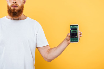 cropped view of bearded man showing smartphone with booking app, isolated on yellow