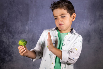 Cute child rejecting broccoli isolated in blue