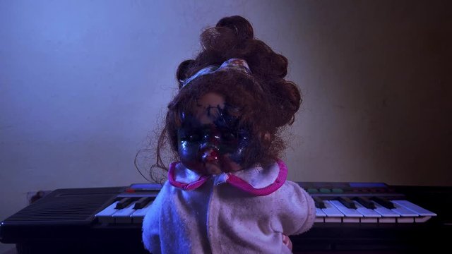 Spooky possessed baby doll playing an innocent tune on the piano and the head turning to reveal a horrifying face staring and smiling at the at the camera