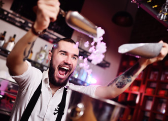 a handsome bearded bartender in a white shirt pours ice for cocktails and screams happily against the bar at a nightclub party