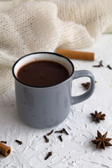 Obraz na płótnie Canvas winter and autumn hot drinks. grey cup of hot chocolate or cocoa and cinnamon, anise star with knitted white plaid on white background. copy space. vertical