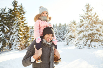 Father with his daughter on his shoulders in the winter in the park