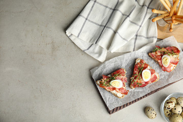 Cutting board of delicious bruschettas with prosciutto on grey table, flat lay. Space for text