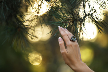 Young woman wearing beautiful silver ring with prehnite gemstone near pine, closeup. Space for text