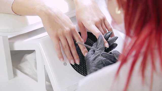 A gloved manicurist woman in a beauty salon nails a client with a nail file before applying a gel coating