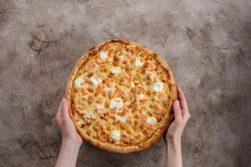 Pizza with salmon and cheese on a textural background. Closeup. Pizza in the hands. The concept of delicious food. View from above.