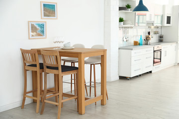Stylish kitchen interior with dining table and bar stools near white wall