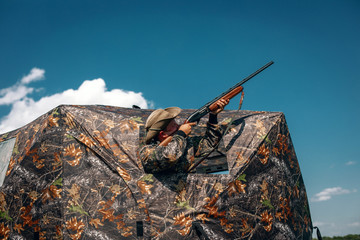Good shot standing in ambush in the khaki tent, aiming to the sky; huntsman concept.