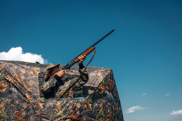 Good shot standing in ambush in the khaki tent, aiming to the sky; huntsman concept.