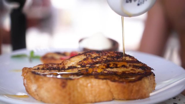 Honey being drizzled over pancakes, waffles, toast or bread in super slow motion.
Served on a white, simple plate with strawberries on top.
