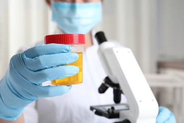 Doctor holding container with urine sample for analysis in laboratory, focus on hand