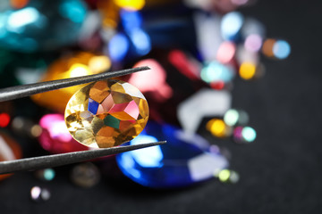 Tweezers with beautiful gemstone on blurred background, closeup. Space for text