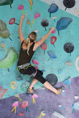 Young woman in climbing equipment moving up while holding by artificial rocks