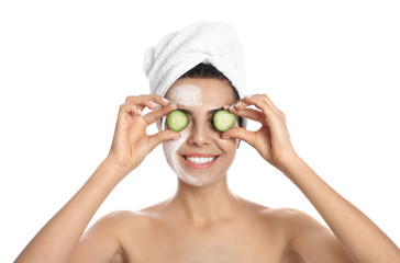 Happy young woman with organic mask on her face holding cucumber slices against white background