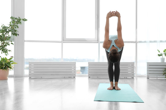 Young woman practicing standing forward bend with shoulder opener asana in yoga studio. Uttanasana pose