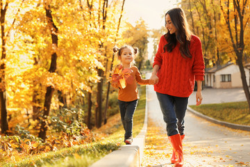 Happy woman with daughter walking in sunny autumn park