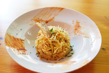 Ball of grated potato with fish and greens on a white plate on a wood table