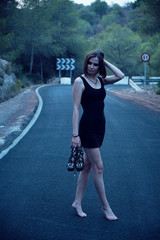 Young woman in a short black dress and sandals along on the forest road