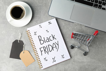 Composition with small shopping cart and notebook on grey background. Black Friday concept