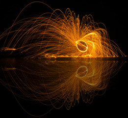 Light lines of steel wool with long exposure and reflection in water. Speed motion abstract background in the dark night. Showers of glowing sparks from spinning steel wool. Long exposure. 