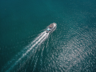 Bird eye view of the white motor boat moving fast, the vessel leaves a beautiful white trace behind; boating concept.