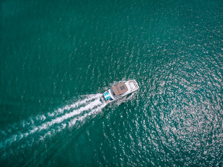 Bird eye view of the white motor boat moving fast, the vessel leaves a beautiful white trace behind; boating concept.