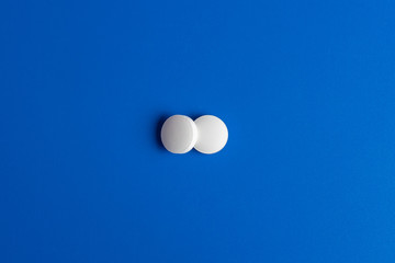 two white round pills on a blue background. Flatlay