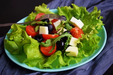 Light salad with tomato greens and cheese on a blue plate.Vegetarian food.