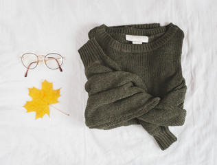 Green sweater and stylish retro glasses isolated on white linen background. Flat lay. Top view.
