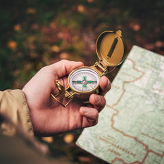 A man holds a compass and a paper map in his hand and is guided by the area, autumn forest, walk,hiking © OlegKovalevich
