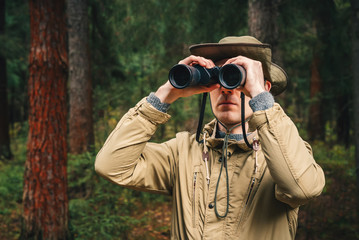 A man in a hat and uniform green and beige holds binoculars and looks into the distance, Ranger...