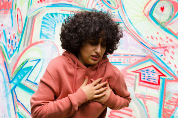 young pretty afro woman looking sad, hurt and heartbroken, holding both hands close to heart,...