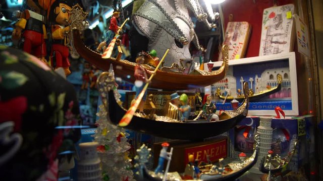 traditional Italian souvenir gondolas with gondoliers sway on Venice shop counter among colourful masks close view