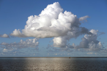 Naklejka na ściany i meble Weiße Wolke vor blauem Himmel im Wattenmeer an der Nordsee vor Hooksiel - Stockfoto
