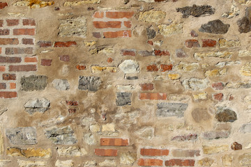 Old wall made of natural rocks and bricks partially coated with plaster