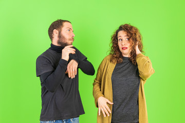 Young beautiful couple on isolated green background with hand on chin thinking about question, pensive expression. Smiling with thoughtful face. Doubt concept.