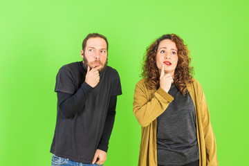 Young beautiful couple on isolated green background with hand on chin thinking about question, pensive expression. Smiling with thoughtful face. Doubt concept.