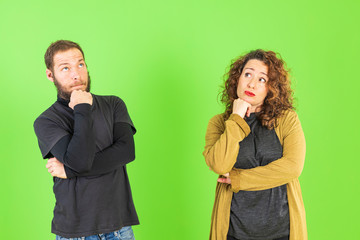 Young beautiful couple on isolated green background with hand on chin thinking about question, pensive expression. Smiling with thoughtful face. Doubt concept.