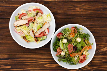 white deep plates with fresh salad ingredients mixed with sauce placed on a rustic background. A place for a menu, banner or advertisement