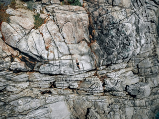 A woman in black swimsuit lying on hot fractured cliffy coast, drone shot, backgroung.