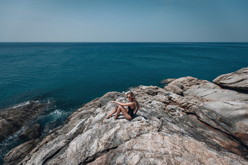 Slim blond woman is on the cliff by the vast blue sea, enjoying the marine; peace, calmness.