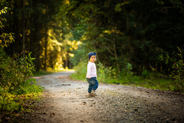 Fototapeta premium Portrait of 2 years old baby girl in forest walking by herself. Not wanting to follow parents.