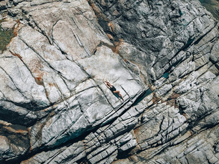 A woman in black swimsuit lying on hot fractured cliffy coast, drone shot, backgroung.