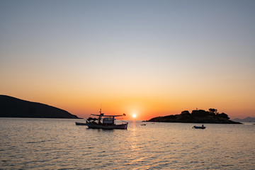 Fototapeta na wymiar fishing boat with greece flag, beautiful sunrise on background