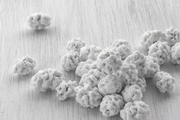 A pile of peanuts in sugar lies on a white wooden background, side view from above