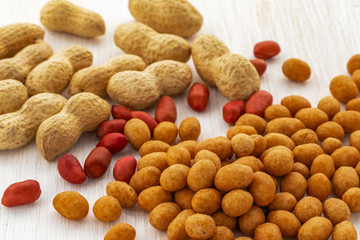 Three types of peanuts are scattered on a white wooden background, side view from above