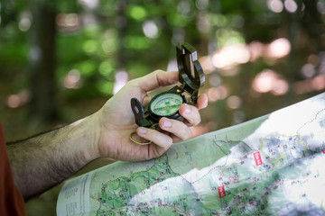 Hiker locating a path in the forest with a compass and a map
