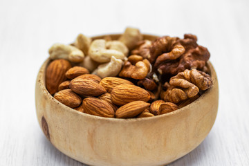 Almonds, cashews and walnuts in a brown wooden bowl on a white wooden background, side view from above