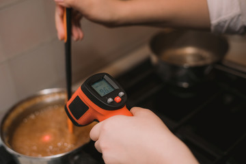The cook measures the temperature of the dish with a special electronic thermometer. Girl measures the temperature of hot caramel