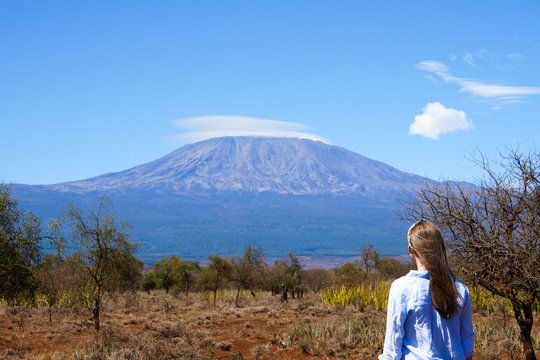 Brown haired girl wearing blue shirt looking at Mount Kilimanjaro. Clear, sunny day. Amboseli, Kenya -Image